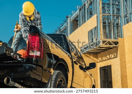 A construction worker loads tools into a truck at a building site on a sunny day.