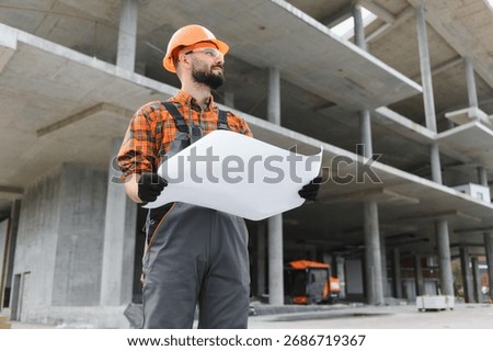 Construction worker looking at building plans, overseeing construction progress at large concrete building site