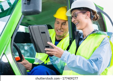 Construction Worker In Construction Machinery Discussing With Engineer Blueprints On Pad Or Tablet Computer On Site