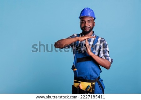 Construction worker making the pause gesture on camera, showing the T-shaped stop sign with arms in the studio. African american builder requesting time out for a short break, wearing hard hat and