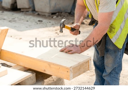 Construction worker making shutter  formwork from timber and plywood for concrete pour using hammer and nails on construction site