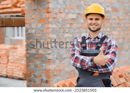 Construction worker man in work clothes and a construction helmet. Portrait of positive male builder in hardhat working at construction site