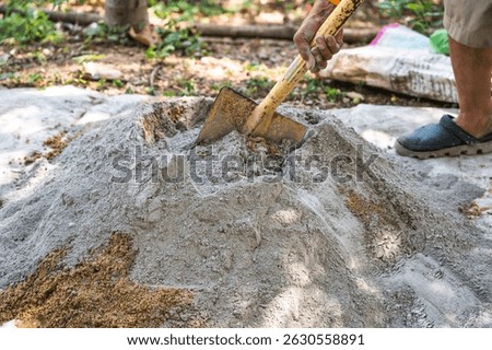 Construction worker manually mixes sand, cement, and water on the ground using a shovel and trowel, following a traditional outdoor concrete preparation method