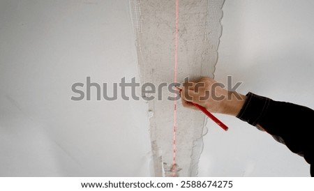 Construction worker marking wall using pencil, laser level and tape measure during home renovation