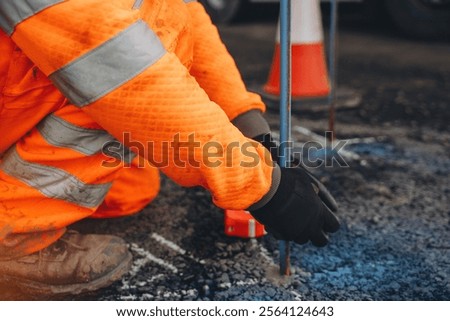 Construction worker measures depth on a road construction site with precision tools during daylight hours