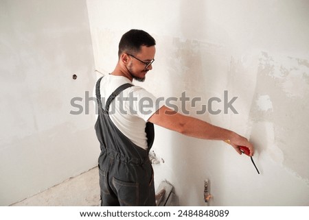 Construction worker measuring wall with tape measure, white background. Back view. Skilled builder using tape measure on white wall.