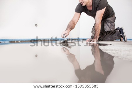 Construction worker mixes leveling compound, putties the floor and prepares the floor for parquet laying