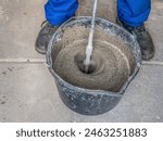 Construction worker mixing mortar in a bucket using handheld concrete mixer