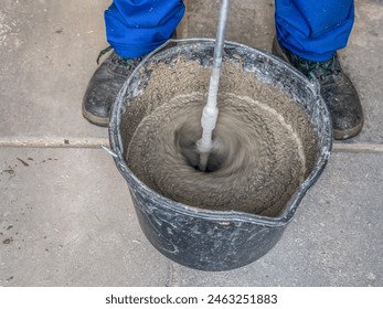 Construction worker mixing mortar in a bucket using handheld concrete mixer