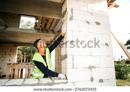 Construction worker monitors build quality, inspects masonry, verifies fit, alignment, and finishing, teamwork action, site control, safety adherence, project task.