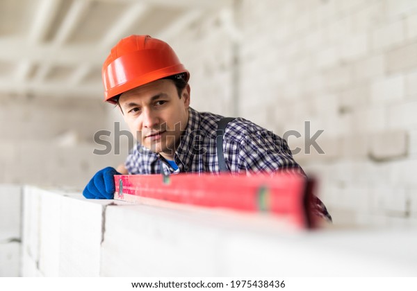 Construction worker observing and surveying wall\
alignment using water\
level