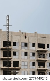 Construction worker on a ladder performing maintenance on a high-rise building facade under a clear sky.