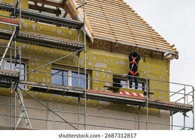 Construction worker on scaffolding installing facade insulation with mineral wool, exterior wall renovation, roof and house building works