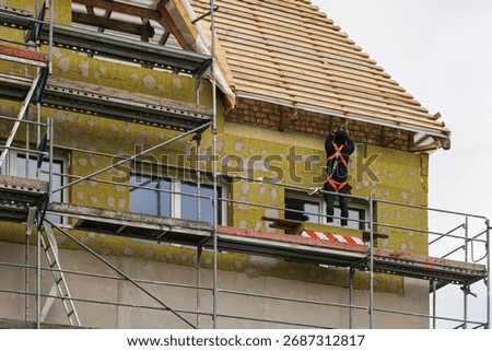 Construction worker on scaffolding installing facade insulation with mineral wool, exterior wall renovation, roof and house building works