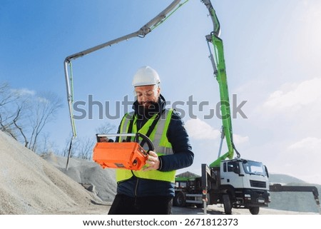 Construction worker operating concrete pump truck remote control at production plant on sunny day