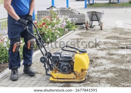 Construction Worker Operating a Plate Compactor on Paved Surface.