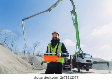 Construction worker operating remote control for concrete pump truck at production plant on sunny day