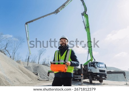 Construction worker operating remote control for concrete pump truck at production plant on sunny day