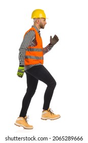 Construction worker in orange reflective waistcoat, lumberjack shirt and yellow helmet is going up the stairs. Side view. Full length studio shot isolated on white.