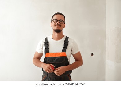 Construction worker in overalls indoor. Smiling young man on white wall background, holding tape measure. cheerful builder with tape measure. - Powered by Shutterstock