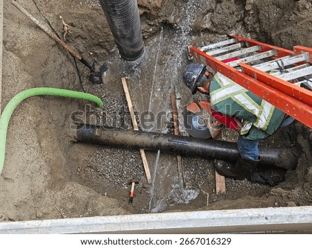 Construction worker overseeing hydro vacuum suction draining water from existing cast iron water main. Utility maintenance, trench safety, and infrastructure repair.