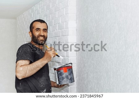 construction worker painter man , brush in hand and buckets of products to restore and paint the wall, indoor the building site of a house