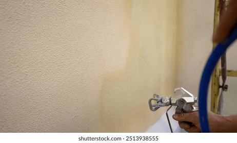 Construction worker painting wall using spray gun.