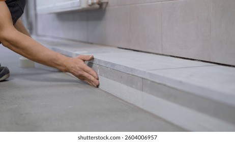Construction worker placing large format tiles on a shower curb, using tile adhesive and mortar