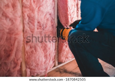 construction worker placing pink insulating foan inside of a wooden frame of a building