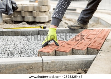 Construction worker placing red concrete paving stones in gravel bed during sidewalk construction