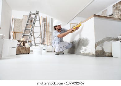 Construction Worker Plasterer Man Uses Caulking Gun In Building Site Of Home Renovation With Tools And Building Materials On The Floor