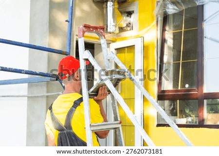 Construction worker portrait with ladder in front of house, home repair project, builder ready for onsite service and maintenance business.