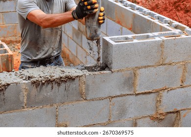 Construction worker pours concrete while laying blocks for new home structure in warm