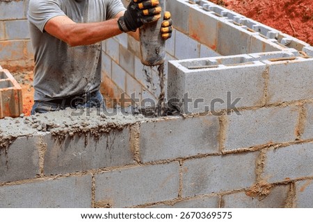 Construction worker pours concrete while laying blocks for new home structure in warm