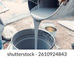 Construction worker pours gray epoxy coating into a bucket, preparing for floor finishing on a construction site