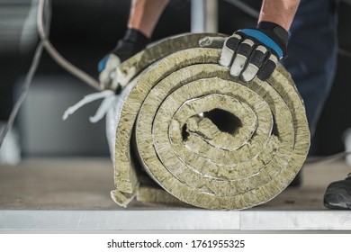 Construction Worker Preparing Roll Of Mineral Wool Insulation To Install Inside Warehouse Wall. Thermal Insulation Systems.