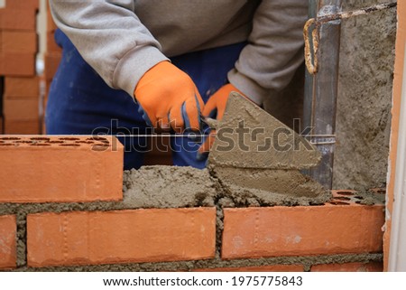 Construction worker putting cement on the brick wall. Man bricklaying. Mason laying bricks.