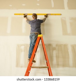 Construction Worker Remodeling Home On Ladder With Level