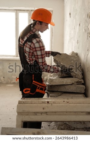 Construction worker removing damaged wall fragments in apartment during renovation. Concept of home repair, demolition, interior remodeling, and improvement process.