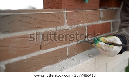 Construction worker is removing excess mortar with a trowel while building a brick wall, ensuring precise and clean bricklaying