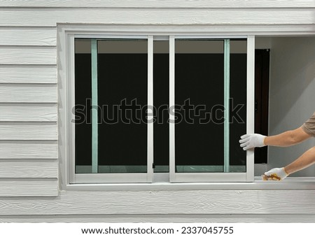 Construction worker repairing the sliding window on artificial woods siding.