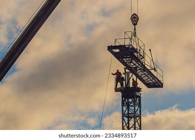 A construction worker rigging with a crane hook at a height against a partially cloudy sky with some out of focus. One of the dangerous work of the world. Fall protection guards installed.