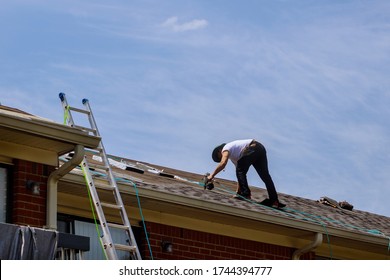 Construction worker roofer builder on roof structure applying asphalt shingles on roofing