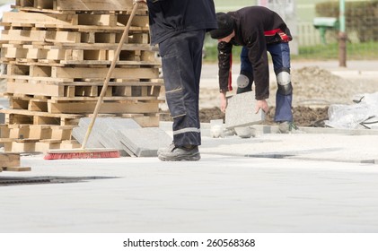 Construction Worker In Safety Clothes Cleaning Building Site After Installing Flagstones In Sand