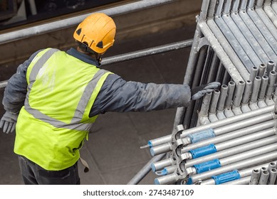 construction worker with safety equipment assembling scaffolding for maintenance of building facade on city street