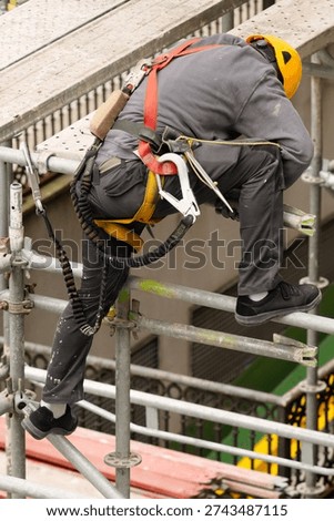 construction worker with safety equipment assembling scaffolding for maintenance of building facade on city street