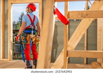 A construction worker in safety gear stands inside a wooden framework, looking up thoughtfully at the structure. The setting is bright with a clear sky. - Powered by Shutterstock