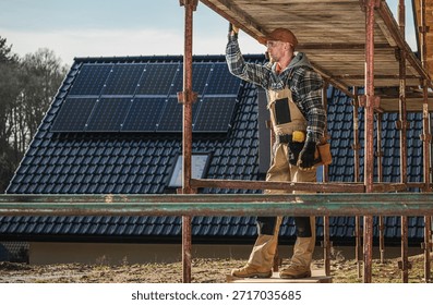 Construction worker is setting up scaffolding at a building site with solar panels on the roof.