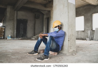 Construction Worker Sitting Sad And Lonely At Job Site Wearing A Medical Mask With Hardhat To Prevent Covid-19 Spreading, Concept Of Unemployment, Economic Crisis Job Loss During Coronavirus Crisis