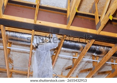 Construction worker skillfully installs spray foam insulation in home renovation on wooden beams structure